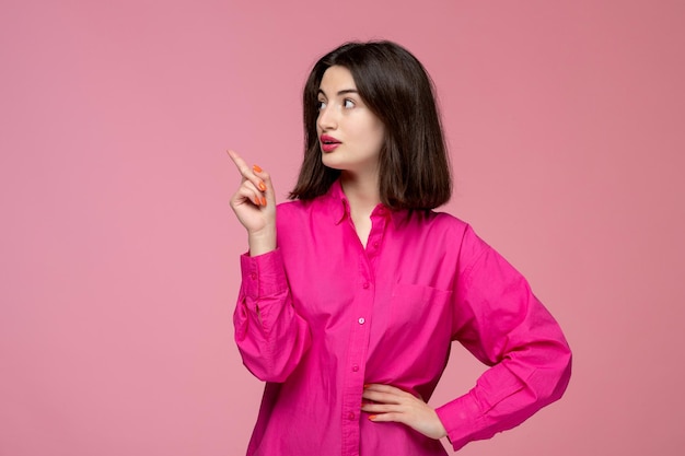 Linda chica encantadora dama adorable con lápiz labial rojo en camisa rosa apuntando a la izquierda