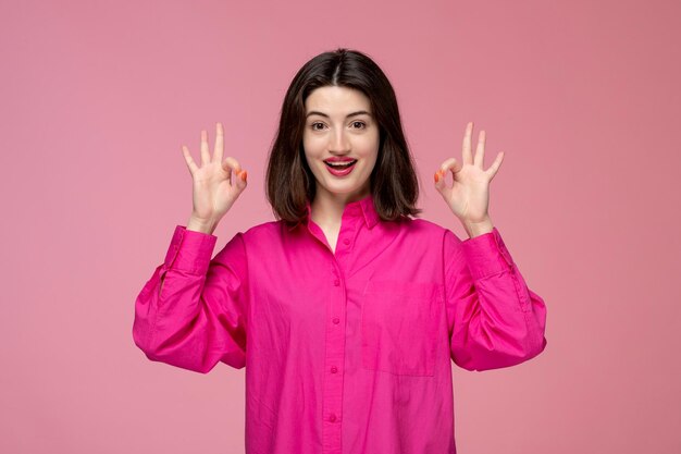 Linda chica encantadora dama adorable con lápiz labial rojo en camisa rosa mostrando signo ok