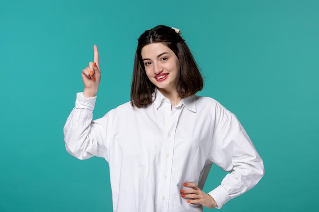 Linda chica encantadora joven bonita chica morena con camisa blanca apuntando hacia arriba feliz