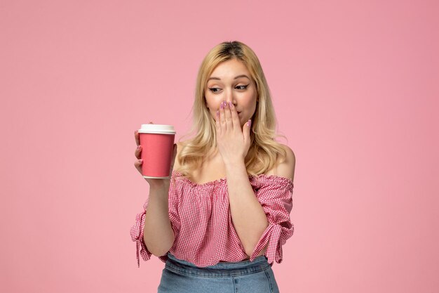 Linda chica encantadora jovencita con lápiz labial rojo en blusa rosa que cubre la boca con taza rosa