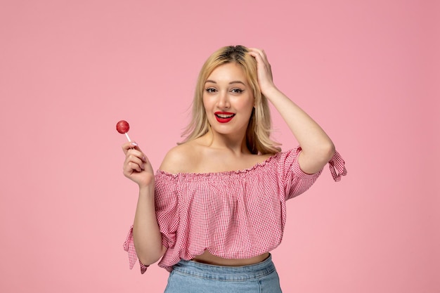 Linda chica encantadora jovencita con lápiz labial rojo en blusa rosa sosteniendo la cabeza y una piruleta rosa