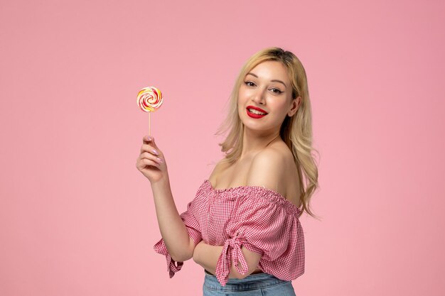 Linda chica encantadora jovencita con lápiz labial rojo en blusa rosa sosteniendo una piruleta dulce de caramelo