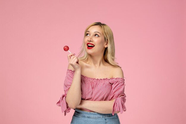 Linda chica encantadora jovencita con lápiz labial rojo en blusa rosa sosteniendo una piruleta rosa redonda