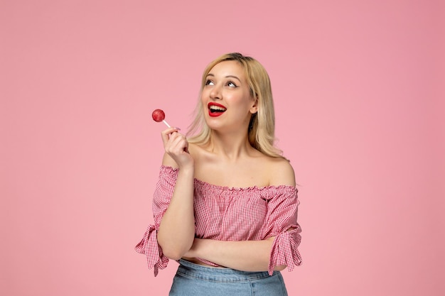 Linda chica encantadora jovencita con lápiz labial rojo en blusa rosa sosteniendo una piruleta rosa redonda