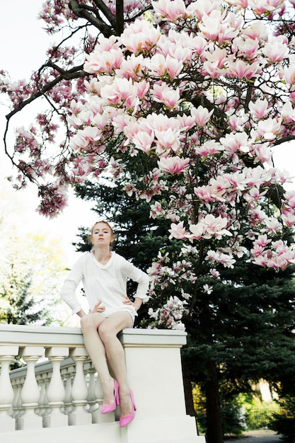 Linda chica está sentada en la barandilla bajo el increíble árbol de magnolia