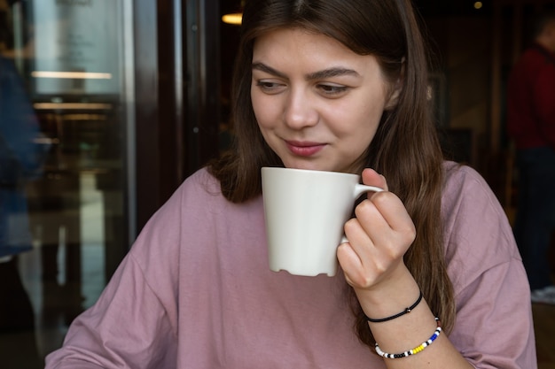 Linda chica de estilo casual con una taza de bebida caliente en un café