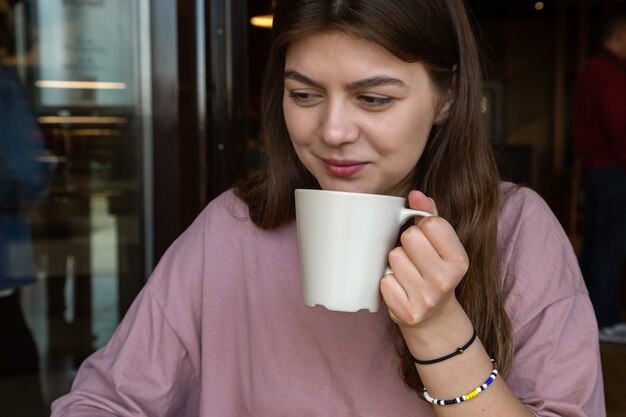 Linda chica de estilo casual con una taza de bebida caliente en un café