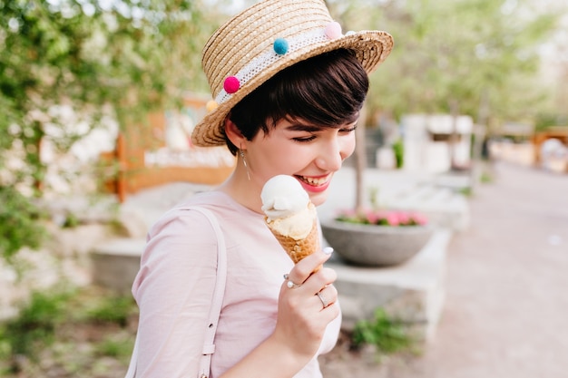 Linda chica feliz con helado dulce en mano pasar tiempo al aire libre, disfrutando de un clima cálido en fin de semana