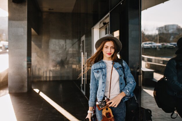 Linda chica guapa con sombrero con expresión de cara encantadora posando afuera mientras el viento juega con su cabello antes de ir de compras.