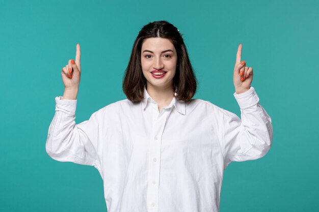 Linda chica joven bastante adorable chica morena en camisa blanca apuntando hacia arriba muy emocionada