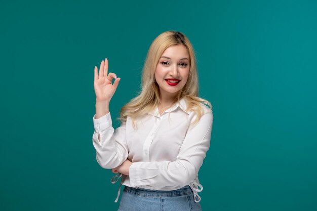 Linda chica joven bastante rubia en una camisa blanca con confianza sosteniendo gesto ok