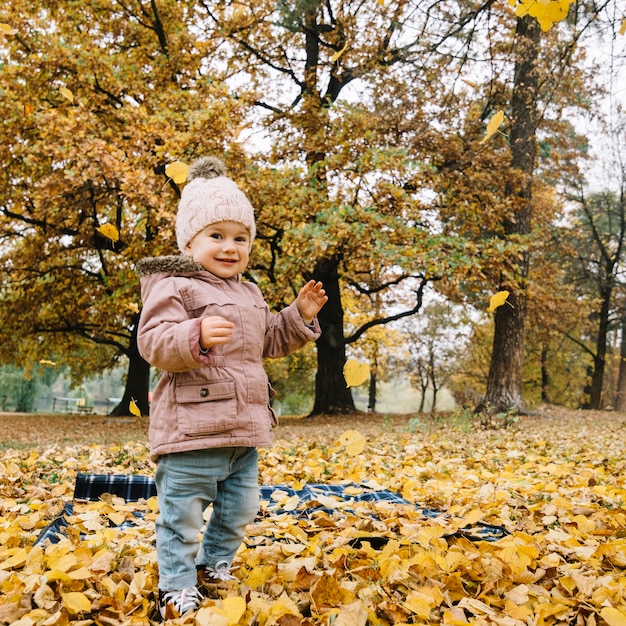 Linda chica lanzando hojas en el bosque de otoño