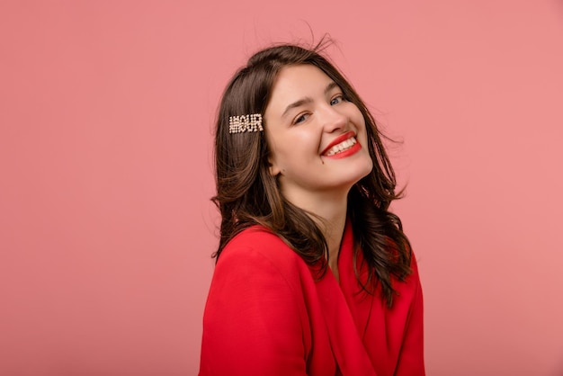 Linda chica morena joven caucásica en chaqueta roja sonríe los dientes a la cámara sobre fondo rosa Estilo de vida diferentes emociones concepto de ocio