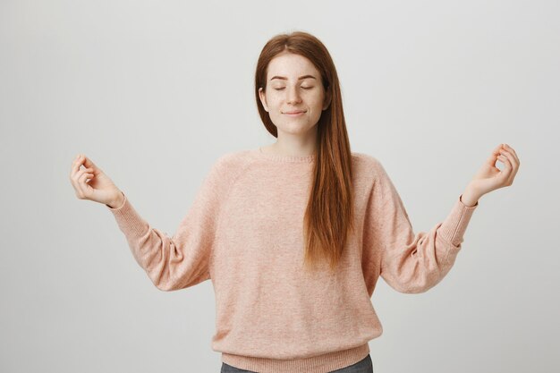 Linda chica pelirroja tranquila meditando, levanta las manos en gesto zen