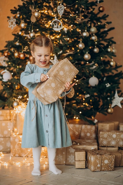 Linda chica de pie con regalos de Navidad junto al árbol