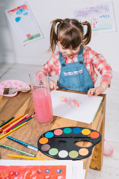 Linda chica pintando con acuarela sobre papel en mesa