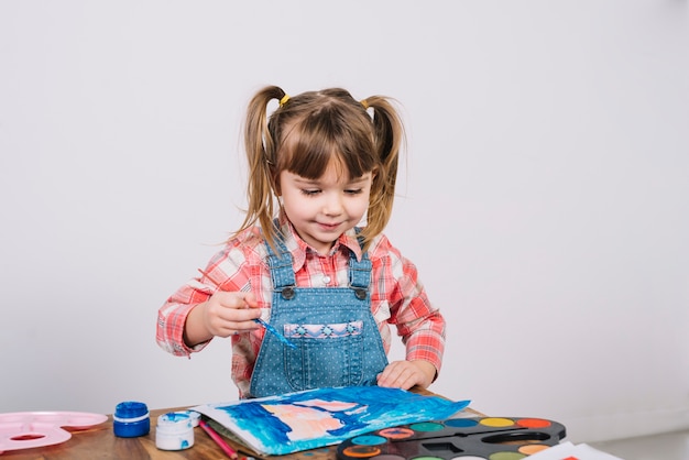 Linda chica pintando con gouache en mesa de madera