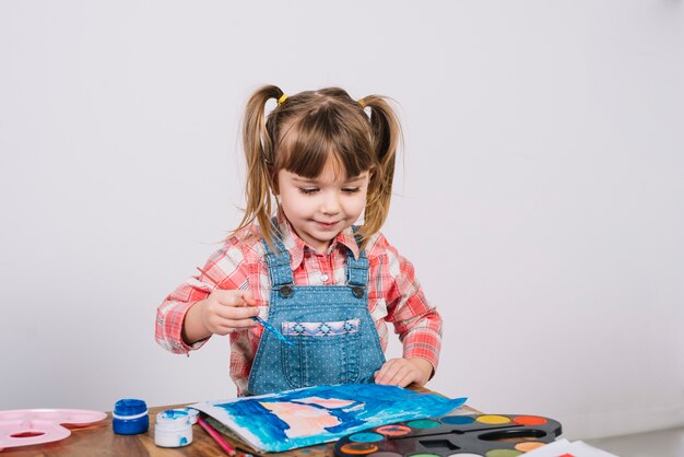 Linda chica pintando con gouache en mesa de madera