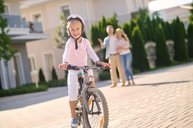 Una linda chica rubia aprendiendo a andar en bicicleta con sus padres.