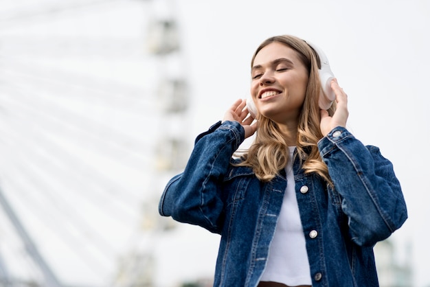 Foto gratuita linda chica rubia escuchando música junto a la noria