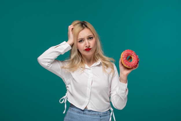 Linda chica rubia hermosa joven con una camisa blanca limpia confundida sosteniendo la cabeza y la rosquilla