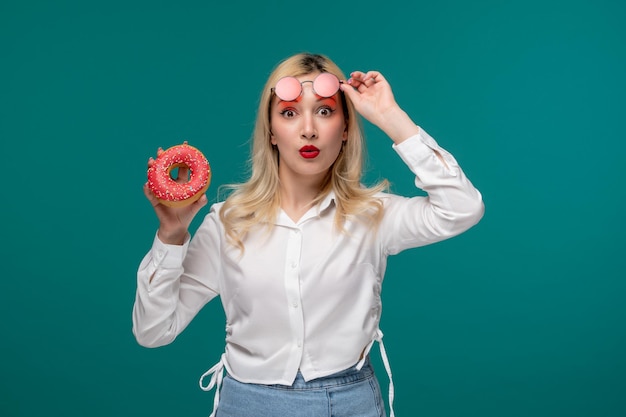 Linda chica rubia hermosa joven en una camisa blanca limpia con gafas de sol rosas con donut