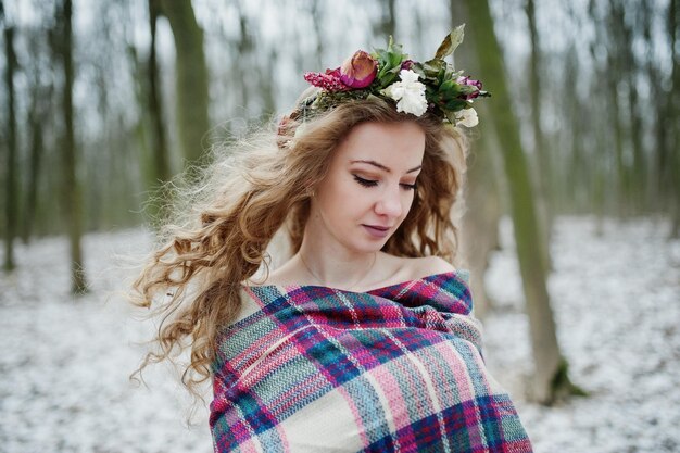 Linda chica rubia rizada con corona en tela escocesa a cuadros en el bosque nevado en el día de invierno