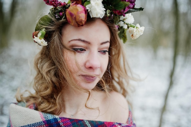 Linda chica rubia rizada con corona en tela escocesa a cuadros en el bosque nevado en el día de invierno