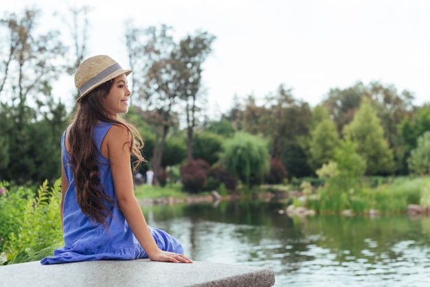 Linda chica sentada junto al lago por detrás