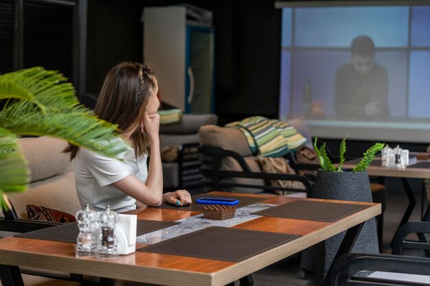 Linda chica sentada en el restaurante y viendo la televisión