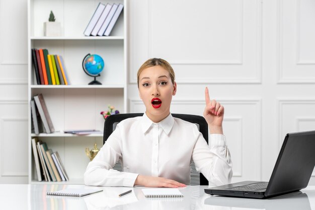 Linda chica de servicio al cliente en camisa blanca con lápiz labial rojo y computadora portátil con una idea emocionada