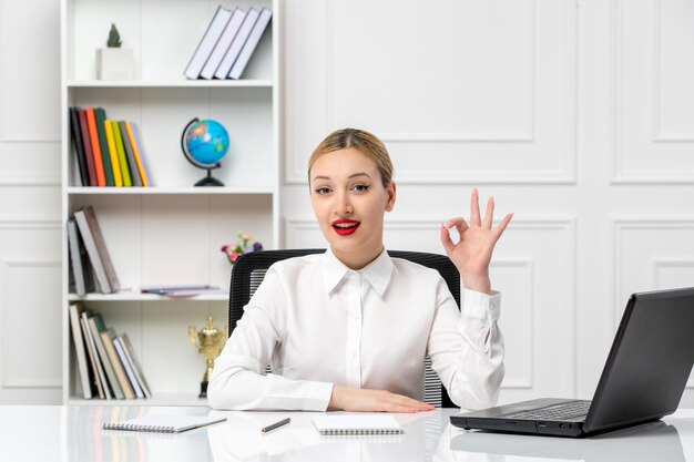 Linda chica de servicio al cliente con camisa blanca con lápiz labial rojo y computadora portátil que muestra un gesto correcto