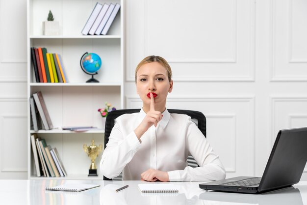 Linda chica de servicio al cliente en camisa blanca con lápiz labial rojo y computadora portátil que muestra el signo de silencio