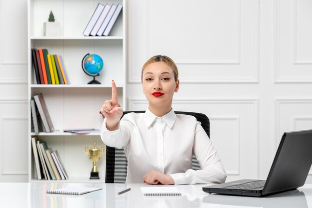 Linda chica de servicio al cliente con camisa blanca con lápiz labial rojo y computadora portátil señalando con el dedo