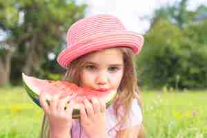 Foto gratuita linda chica con sombrero rosa comiendo sandía rebanada en el parque