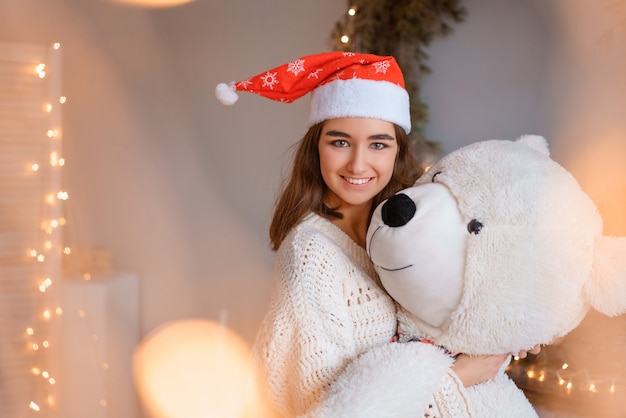 Linda chica con sombrero de Santa sosteniendo un oso de juguete