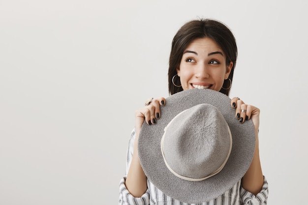 Linda chica soñadora mirando a la izquierda con tentación y morder el sombrero emocionado, sonriendo con alegría