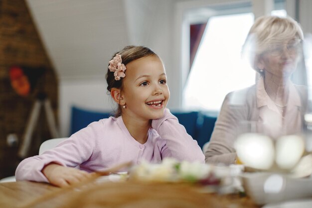 Linda chica sonriente disfrutando de una comida con su abuela en el comedor