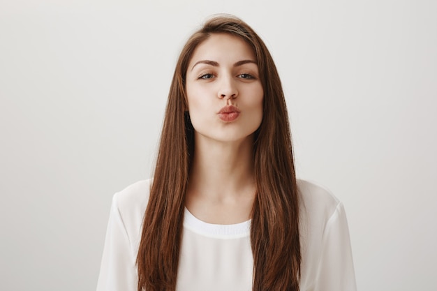 Linda chica sonriente doblando los labios y apoyándose en un beso