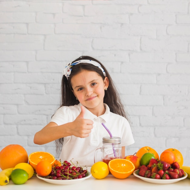 Linda chica sonriente con frutas coloridas mostrando pulgar arriba signo