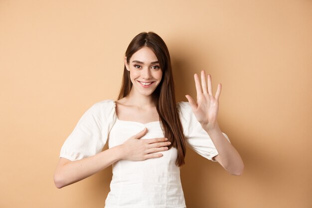 Linda chica sonriente hace promesa poner la mano en el corazón y decir la verdad siendo honesto jurando que estás de pie ...