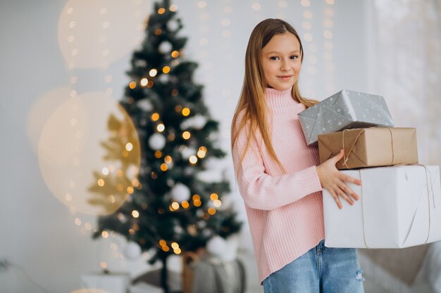 Linda chica sosteniendo regalos de Navidad por árbol de Navidad