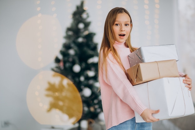 Linda chica sosteniendo regalos de Navidad por árbol de Navidad