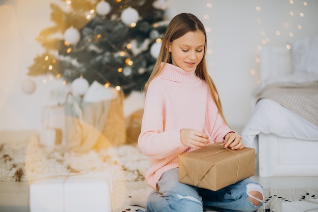 Linda chica sosteniendo regalos de Navidad por árbol de Navidad