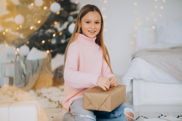 Linda chica sosteniendo regalos de Navidad por árbol de Navidad