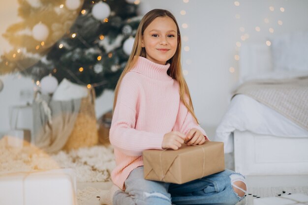 Linda chica sosteniendo regalos de Navidad por árbol de Navidad