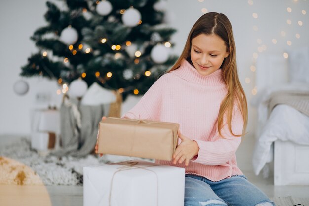 Linda chica sosteniendo regalos de Navidad por árbol de Navidad