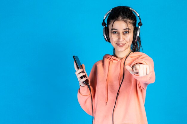 Linda chica sosteniendo el teléfono y señalando con el dedo a la cámara Foto de alta calidad