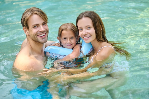 Linda chica y sus padres pasan tiempo en la piscina