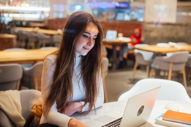Linda chica trabaja en la computadora portátil en la cafetería hipster